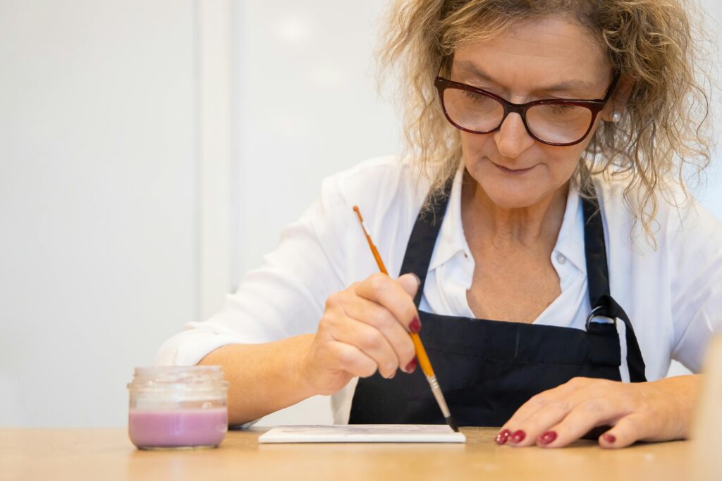 Focused elderly woman painting a ceramic tile, expressing creativity and skill.